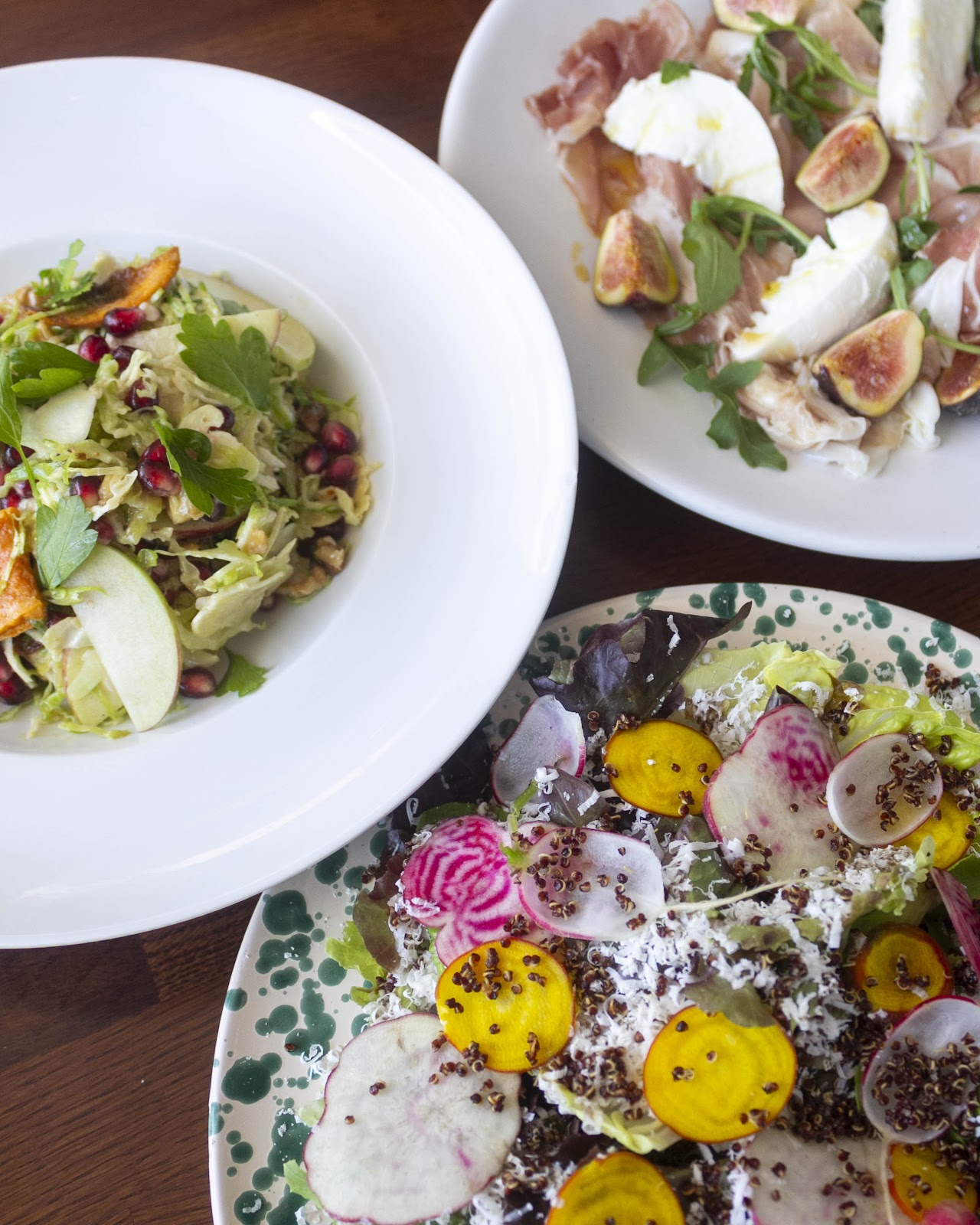 A trio of plates at Trattoria Trullo: figs and prosciutto with burrata, apple-pomegranate slaw, and a beet-radish salad on a green-spotted plate