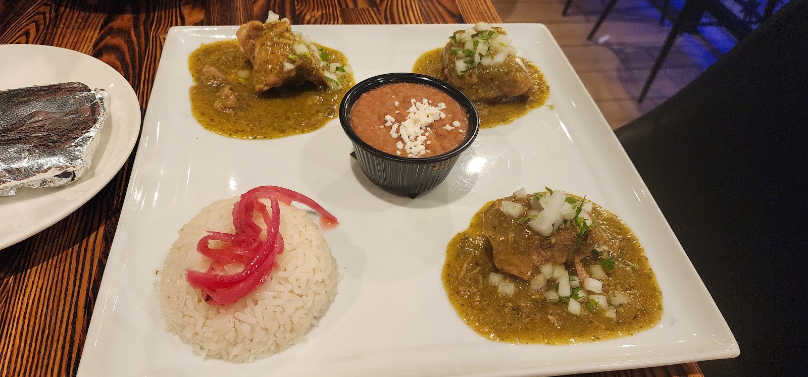 Pork chile verde at Xclusive Mexican Kitchen: tender pork in green salsa with white rice topped with pickled onion and a side of refried beans