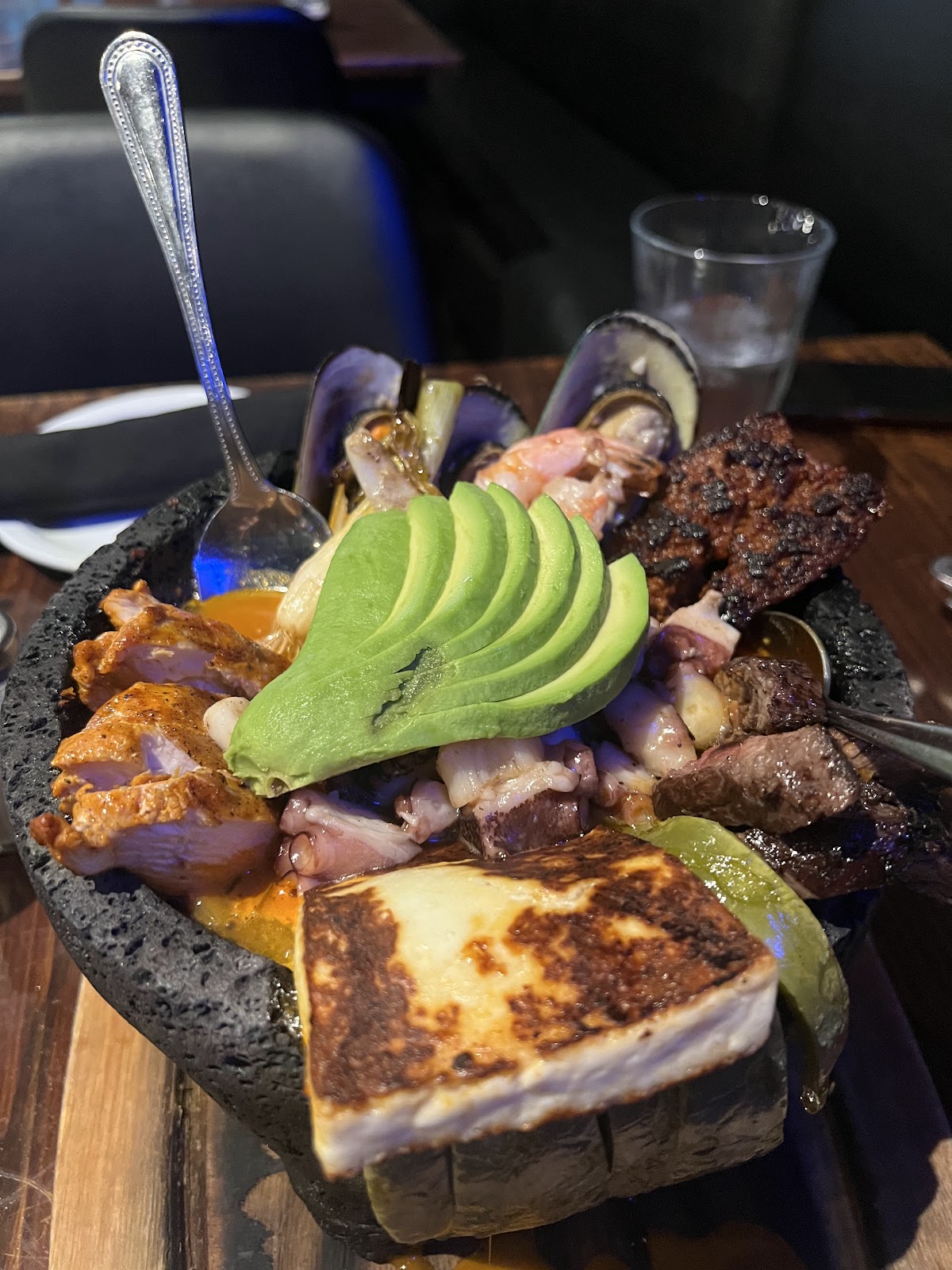 A volcanic-stone molcajete from Xclusive Mexican Kitchen loaded with seafood, grilled meats, a fanned avocado and a slab of grilled queso